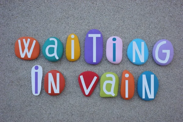 Waiting in vain, negative message composed with multi colored stone letters over beach sand