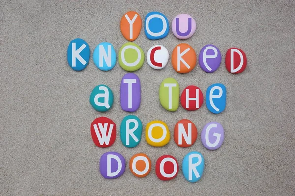 You knocked at the wrong door, creative text composed with hand painted multi colored stone letters over beach sand