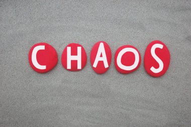 Elle boyanmış kaos kelimesi yeşil kumların üzerine çok renkli taş harfler.