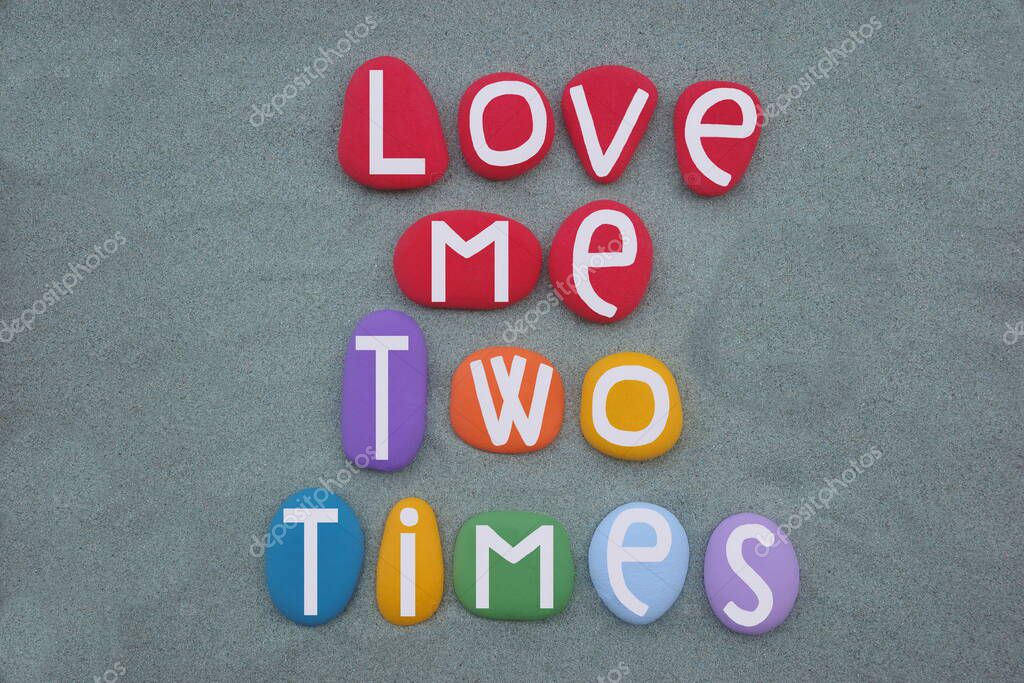 Love me two times, creative message composed with hand painted multi colored stone letters over green sand