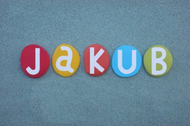 Jakub, masculine given name composed with hand painted multi colored stone letters over green sand clipart