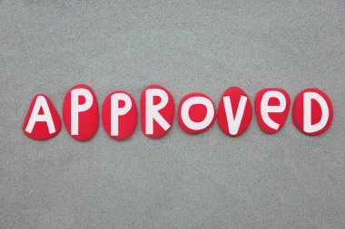Onaylandı, resmi olarak kabul edildi veya tatmin edici olarak kabul edildi, kırmızı metin yeşil kumların üzerine elle boyanmış taş harflerle oluşturuldu.