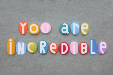 Sen inanılmaz, yaratıcı ve motive edici bir metinsin. Elle boyanmış, yeşil kumların üzerine çok renkli taş harfler.