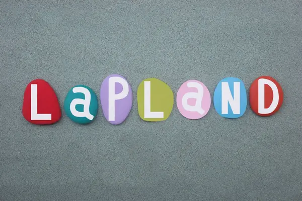 Stock image Lapland, the largest and northernmost region of Finland, souvenir composed with hand painted multi colored stone letters over green sand