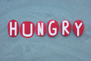 Aç, yaratıcı, yeşil kumların üzerine elle boyanmış kırmızı renkli taş harfler.