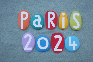 Paris 2024, creative logo composed with hand painted multi colored stone letters over green sand