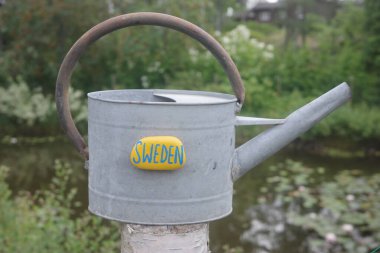 Sweden stone magnet on a metallic watering can in a garden clipart