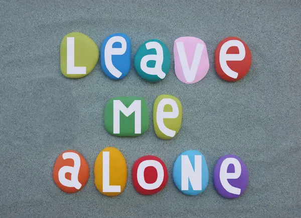 stock image Leave me alone, creative slogan composed with hand painted multi colored stone letters over green sand