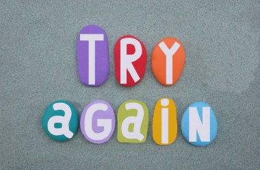 Tekrar dene, yeşil kumların üzerine elle boyanmış çok renkli taş harflerle oluşturulmuş yaratıcı logo.