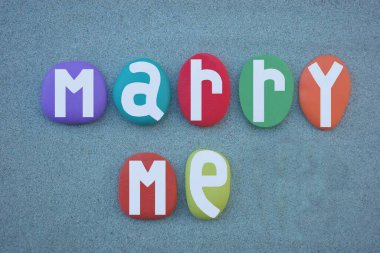 Evlen benimle, yeşil kumların üzerine çok renkli taş harflerle yazılmış yaratıcı aşk mesajı.