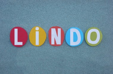 Dört İber Yarımadası dilinde güzel, güzel anlamına gelen Lindo, Portekizce, Kastilya, Katalan ve Galiçya dili, çok renkli taş harflerle yeşil kumların üzerine yazılmış yaratıcı metin.