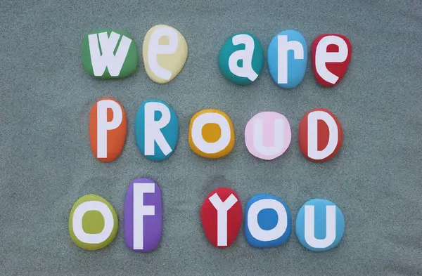 Seninle gurur duyuyoruz, motivasyon sloganı ve yeşil kumların üzerine çok renkli taş harflerle yazılmış mesaj.