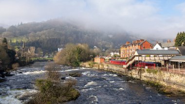 Looking up the river Dee at llangollen. In the distance the low cloud is covering the hills. The train station is to the right with carriages visible. clipart