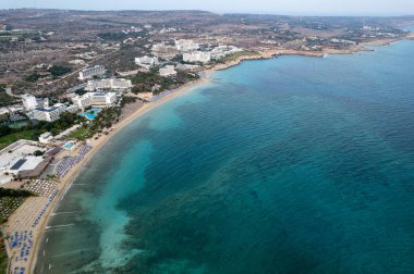 Kıbrıs Rum Kesimi 'nin Ayia Napa adlı organize plajlı kıyı şeridi manzarası. Güneşlenen güneş yatakları ve şemsiyeleri olan altın kumlu sahillerin insansız hava aracı manzarası