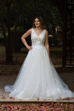 Beyaz gelinlikli, mutlu, hamile gelin dışarıda poz veriyor.