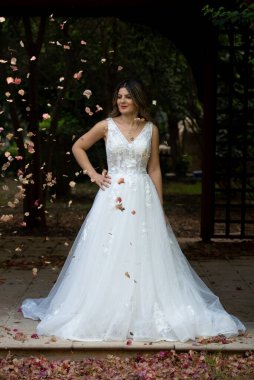 Beyaz gelinlikli, mutlu, hamile gelin dışarıda poz veriyor.