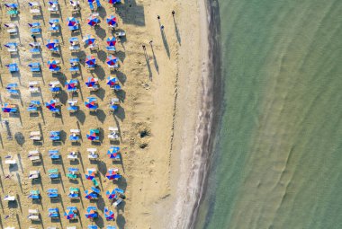 Renkli şemsiyeli kumlu sahil manzarası, yazın güneşli bir günde şeffaf mavi suyla körfezde yürüyen insanlar. Larnaka ve Kıbrıs seyahati