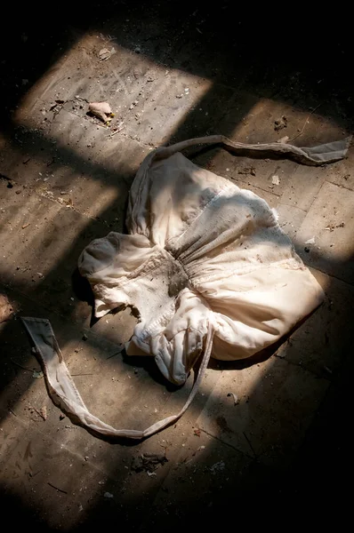 汚れた床の上に古い汚れた白い子供のドレス 明るい太陽の光が窓に入る 放棄された場所 — ストック写真