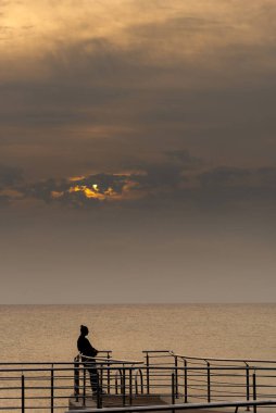 İskelede tek başına duran kişi denizde dramatik günbatımının tadını çıkarıyor.
