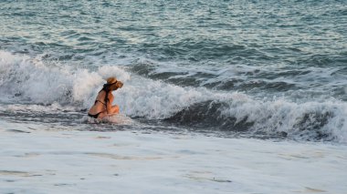Unrecognized Woman sitting on a sandy beach in the afternoon with windy waves. Paphos Cyprus