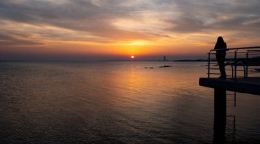 Person standing alone on a pier enjoying dramatic sunset at the sea.