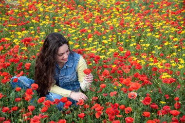 Young woman laying down in a daisy poppy field smiling in spring.