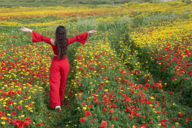 Attractive young woman wearing red dress walking happy in poppy flower spring field. Springtime Cyprus