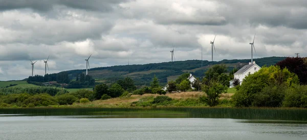 白いコテージの家と風力代替エネルギーのための風車を持つアイルランドの田舎 — ストック写真