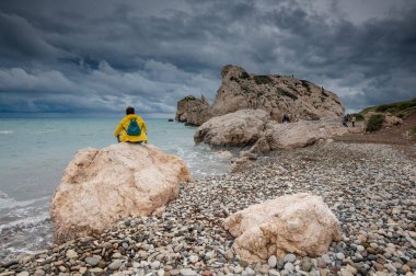 Kışın deniz manzarasının tadını çıkaran bir kadın. Fırtına bulutları, Afrodit Kaya Paphos Kıbrıs