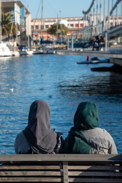 stock image Muslim women wearing traditional head scarf sitting and sightseeing at the marina on Barcelona in Spain. Travel in Europe.