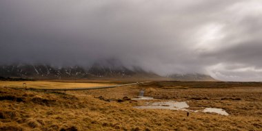 İzlanda kırsalında karada yosun, baharda boş yol ve kar dağları.