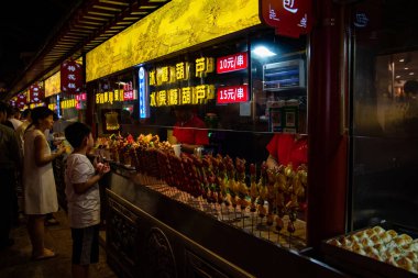 Pekin, Çin, Haziran 12018: Çinliler geceleri bir sokak şekerleme dükkanından şeker satın alıyorlar. Atıştırmalık sokak yiyecek pazarı Pekin porseleni