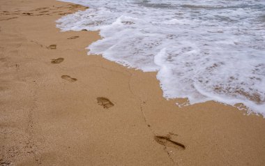 Kumsalda ayak izleri ve sahilde dalgalar..