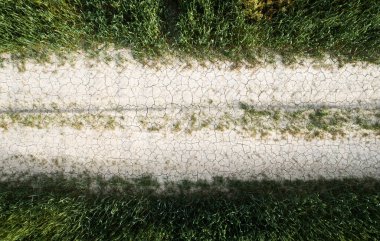 İkincil kuru kırsal yolun insansız hava aracı manzarası bir tarla çayırını geçiyor..