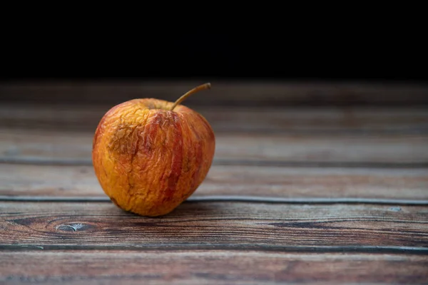 stock image Red wilted rotten apple on a table. Bacteria infected rotten fruit.