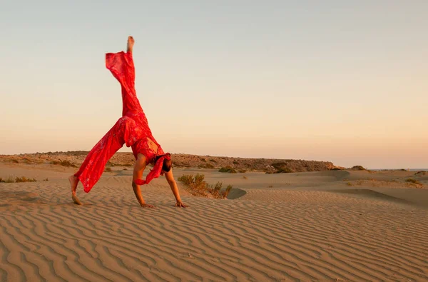 若いです魅力的な女性身に着けていますで赤い抜粋で砂の砂丘で砂漠に対して青い空 — ストック写真