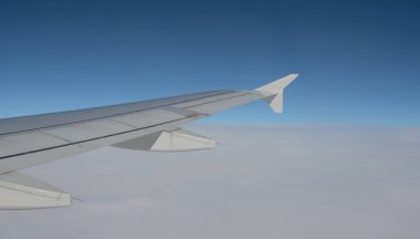 Uçak uçuyor. İnsanlar seyahat ediyor. Uçak penceresinden hava görüntüsü. Bulutların üstündeki mavi gökyüzü.