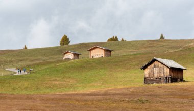 Windy Road dağ evi ahşap evler ve dışarıda yürüyüş yapan insanlar. Aple di siusi Seiser İtalyan Alpleri.