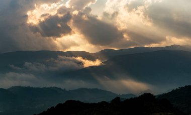 Parlak güneş ışınları gün batımında karanlık bulutların üzerinde parlıyor. Kışın dramatik gökyüzü.