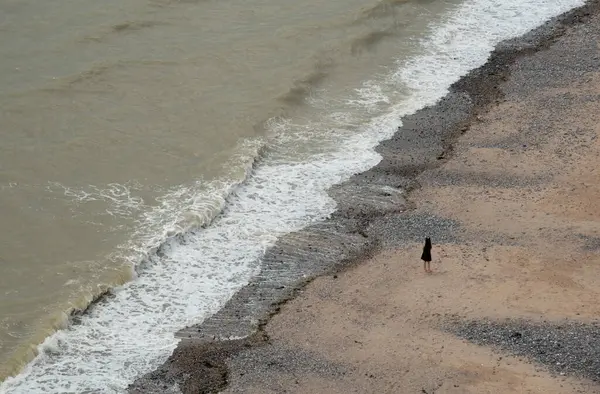 Denizin kıyısında duran tanınmamış genç kız. Rüzgarlı dalgalar Atlantik okyanusu. Okyanusta aktif insanlar