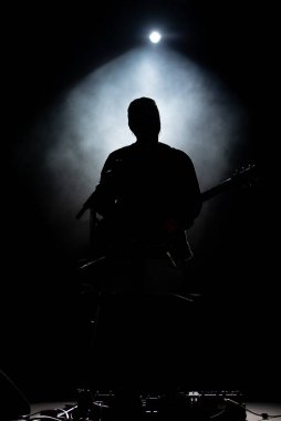 Sahnede bir gitaristin silueti çalıyor. Sahne arkası ışıkları. Konserde müzik çal .