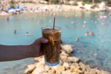 Sahilde insan eli soğuk kahve bardağını tutuyor. Yaz tatilleri