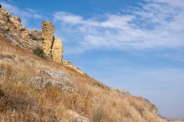Kuru bir uçurumun yamacında doğal kaya oluşumu. Bulutlu mavi gökyüzü kopyalama alanı