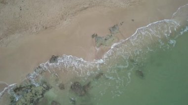 Kumlu bir plaja düşen okyanus dalgalarının 4K hava görüntüsü. Kumsalda deniz dalgaları fren yapıyor. Altın kumlu tropikal plaj.