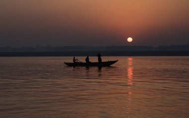 Güneş doğarken Ganj nehrinde tahta bir teknede turistler. Varanasi Hindistan.