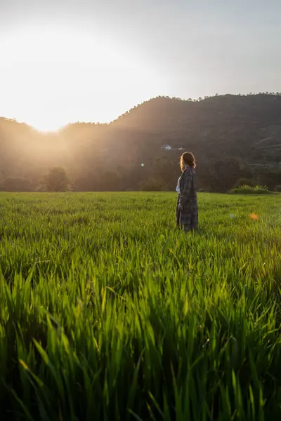 Woman with long coat holding long hair enjoying sunset on the green meadow. People active outdoor