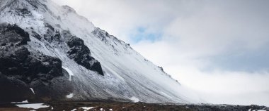 Baharda ince kar tabakası ve bulutlu gökyüzü ile kaplı İzlanda panoramik manzarası. Snaefellsnes Yarımadası İzlanda. Siyah dağ