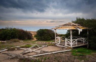 Terk edilmiş bir sahil kulübesi ve terk edilmiş bir bahçe. Terk edilmiş yıkılmış binalar. Fırtınalı bulutlu gökyüzü.