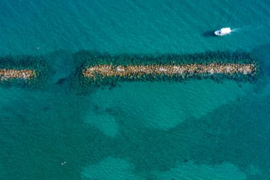 Motorlu aracın zümrüt yeşili okyanus suyunu taştan dalgakıran hava manzarası yakınlarından geçerken görüntüsü. Paphos Kıbrıs