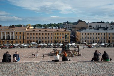 Helsinki, Finlandiya, 18 Temmuz 2024: Helsinki, Finlandiya 'da güneşli bir yaz gününün tadını çıkaran turistler ve arka planda hükümet sarayı bulunuyor.